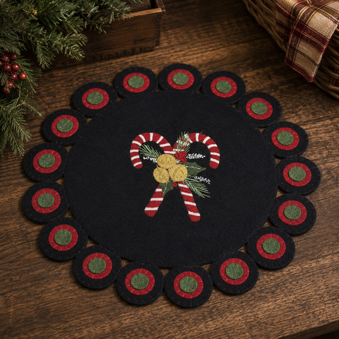 Black Christmas candle mat with crossed candy canes, greenery, berries, and bells on a decorative scalloped border.