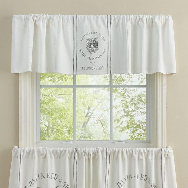 White farmhouse seed sack valance with vintage grain sack style print hanging above a bright country kitchen window.