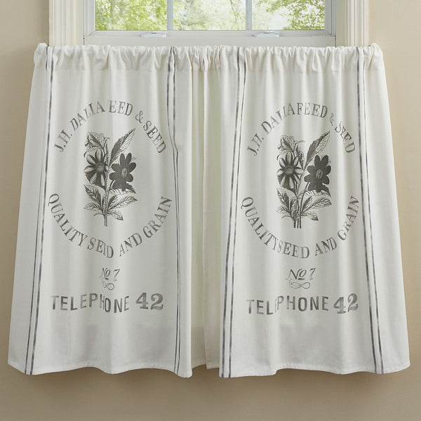White farmhouse seed sack tier curtains with vintage grain sack print hanging in a bright country style kitchen window.