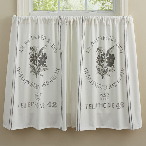 White farmhouse seed sack tier curtains with vintage grain sack print hanging in a bright country style kitchen window.