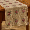 Granny Square 13x36 crochet table runner in cream with muted rose and sage green floral squares on a rustic wood table