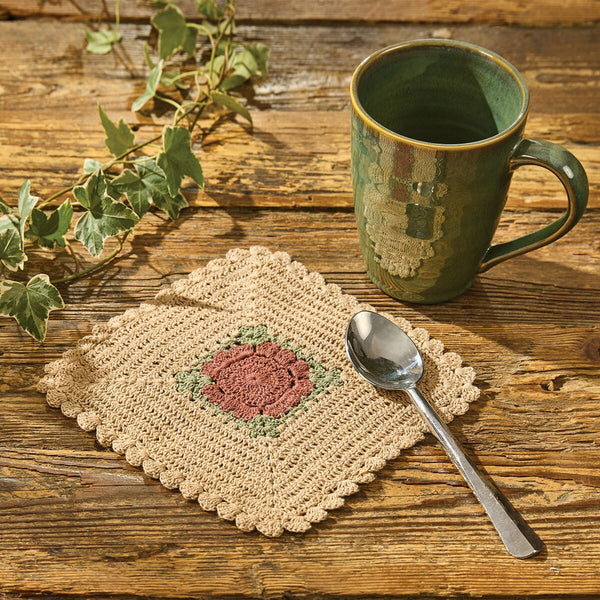 Granny Square 8x8 crochet trivet in cream with muted rose and sage green center on a rustic country table