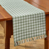 Primitive ivy green and cream plaid Stafford farmhouse table runner with fringe displayed on a wooden country table.