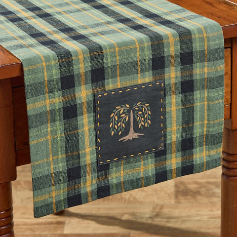 Add rustic charm with the Willow Lane Plaid Table Runner. Features green, gold, and black plaid with a stitched willow tree patch. Perfect for farmhouse dining.