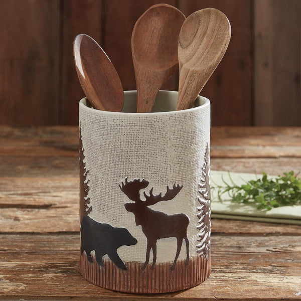 The Wilderness Trail Utensil Crock brings a charming touch of the wilderness to your kitchen and adds a rustic feel! Complete the look with the coordinating kitchen linens and tableware!  Colors: Chocolate, Candlelight White, Cast Iron, Light Nutmeg & Nutmeg Dimensions: 6.75" H x 5.75" Diameter