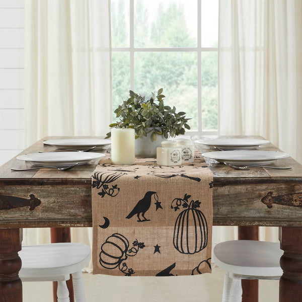 The Raven Harvest Burlap Jute Runner measures 12 by 36 inches and features a woven burlap base in natural tan. The textured Thanksgiving table runner features a whimsical pattern with stenciled black pumpkins, crows, stars and crescent moons.