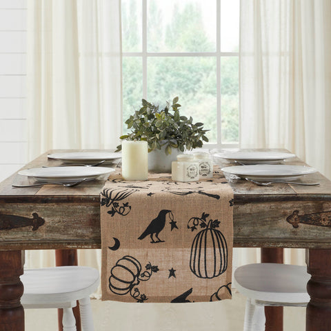 The Raven Harvest Burlap Jute Runner measures 12 by 36 inches and features a woven burlap base in natural tan. The textured Thanksgiving table runner features a whimsical pattern with stenciled black pumpkins, crows, stars and crescent moons.