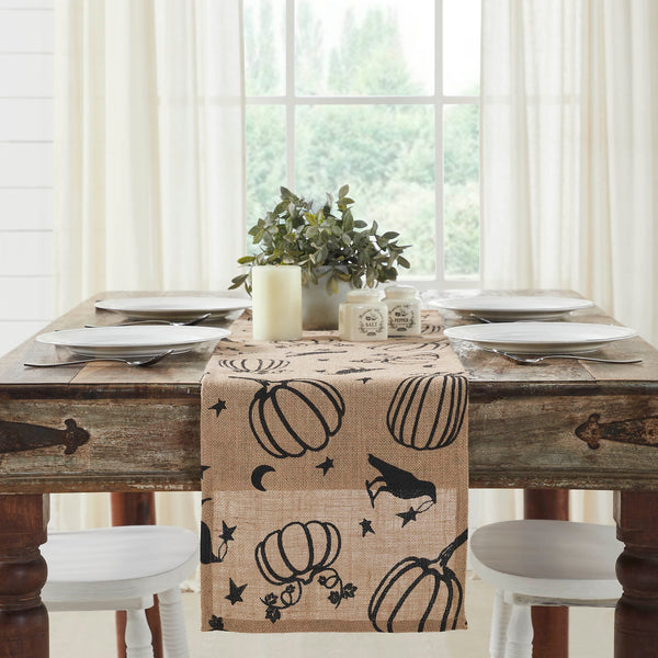 The Raven Harvest Burlap Jute Runner measures 12 by 48 inches and features a woven burlap base in natural tan. The textured Thanksgiving table runner features a whimsical pattern with stenciled black pumpkins, crows, stars and crescent moons.