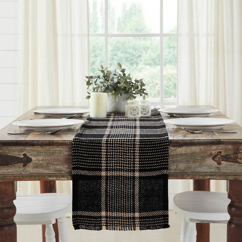 Give your tabletop decor a seasonal upgrade with traditional plaid in deep tones. The Eston Black Tan Runner measures 12 by 60 inches and features a woven base in recycled cotton with frayed edging. The dark fall table runner features a black base with deep tan striping. Pair with other pieces from the Eston Black Tan Plaid Collection by VHC for a timeless farmhouse look.