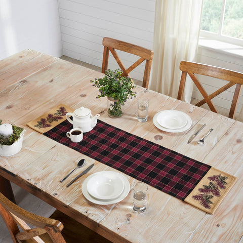 Give your tabletop decor a seasonal upgrade with traditional plaid in deep tones with pinecone accents. The Connell Pinecone Runner measures 12 by 48 inches and features a woven base in 100 percent cotton. The dark fall table runner features a burgundy and black plaid base flanked by tan blocks featuring a primitive pinecone and pine needle design
