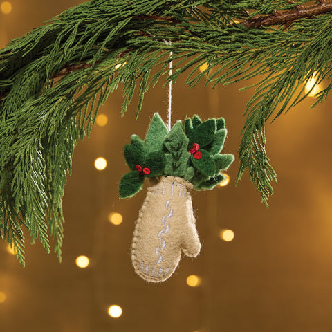 Mittens Felt Ornament is a felt ornament in the shape of a beige mitten filled with holly. The mitten is accented with white embroidery and the holly with red buttons for holly berries. Item is slightly filled for a weighted feel. Includes a string for hanging on the Christmas tree.