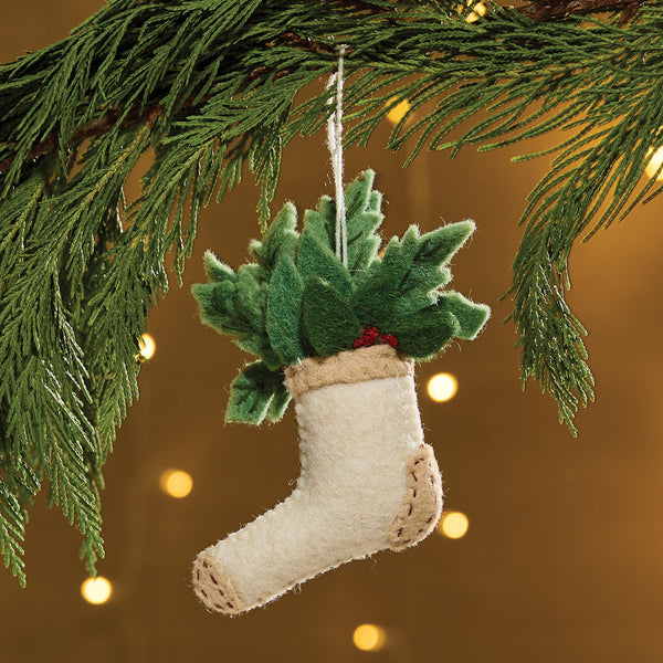 White Socks Felt Ornament is a felt ornament depicting a sock filled with holly and berries. It is accented with a heal and toe patches and small read buttons as holly berries. Item is slightly filled for a weighted feel. Includes a string for hanging on the Christmas tree.