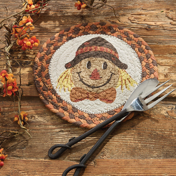 Round scarecrow printed trivet with fall colors on rustic wood table with serving utensils