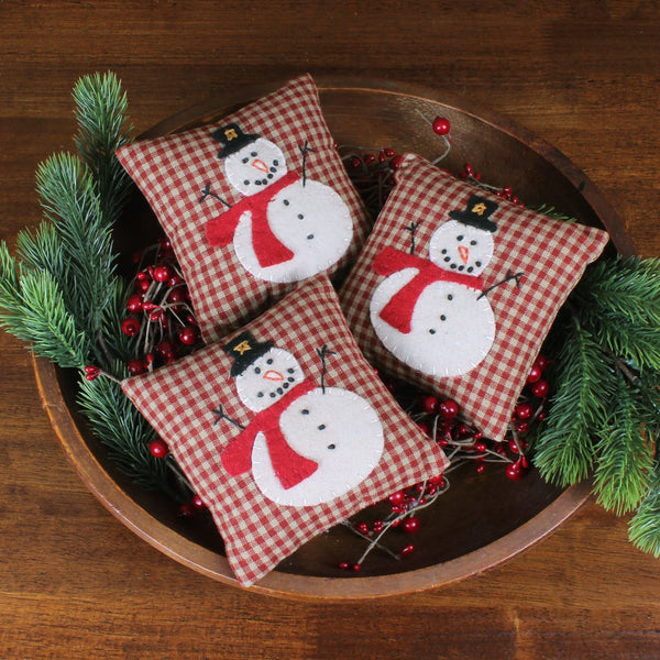 Primitive snowman bowl fillers on brown homespun check fabric displayed in a wooden dough bowl with holiday greenery.