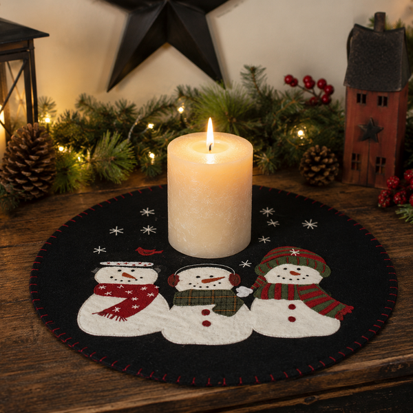 Snow Friends Candle Mat featuring three embroidered snowmen beneath a snowy winter sky on a black wool felt background.