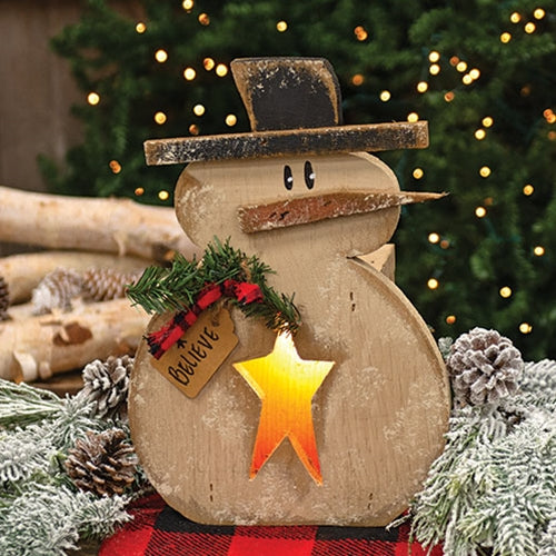 Rustic Wood Light Up Believe Snowman with glowing star cutout, black hat, greenery accent, and primitive Christmas styling displayed on a tabletop.