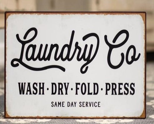 Laundry Co metal sign has a white background with black lettering stating "Laundry Co Wash Dry Fold Press Same Day Service". Edges of the 13-3/4" H x 10-1/4" W sign are distressed for a vintage look. There are two sawtooth hangers on the back for stability when hanging.