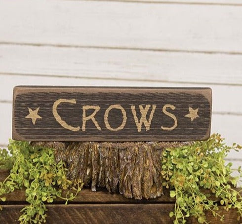 The Crows Barnwood Sign is a decorative sign made of raw natural wood with softly worn edges. The sign has a distressed black paint finish and reads “Crows” in rustic ivory lettering with star graphics, making it a fun and festive addition to the home for the Halloween season.