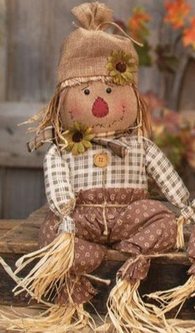 The 26.5" Edgar Scarecrow is a primitive doll in a scarecrow design perfect for accenting country fall looks. He wears a burlap hat, brown trousers with a jute rope belt, and a plaid scarf with a flower accent. His face has primitive stitching and his hair and limbs are made of raffia.