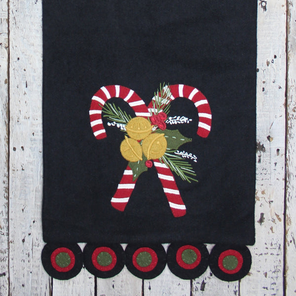 Candy Canes Black Table Runner featuring embroidered candy canes, greenery, berries, and golden bells on a black wool felt background with decorative scalloped ends.