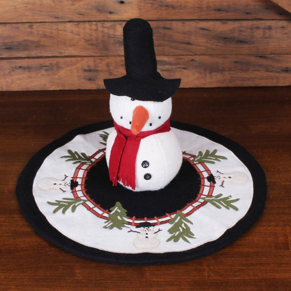 Home For The Holidays Candle Mat featuring embroidered snowmen, evergreen branches, and a rustic wreath design on wool felt for Christmas decorating.