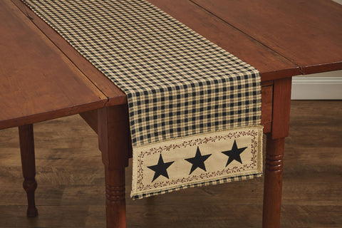Enhance your dining decor with this charming Star Patch Table Runner! The bold black & sand plaid pattern is enhanced with a frayed homespun patch on both ends. The patch is accented with an appliqued black star surrounded by a vine-and-berry motif - a classic country design! So versatile, use throughout your home as an accent mat for you favorite candle/decorative pieces, on a mantel, or wherever your creativity leads you!   Colors: Black, Sand & Cranberry