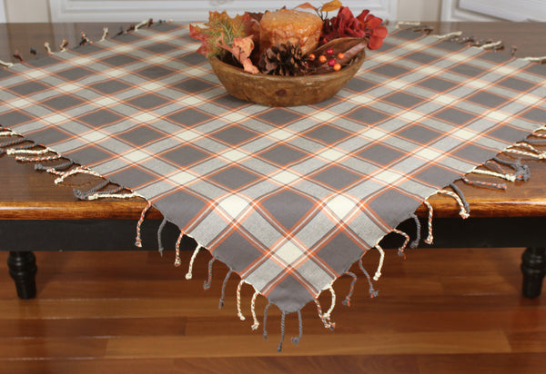 Our gray Fall Sky Table Square featues a plaid of gray, orange, and cream and measures 36"x36" with a hand braided fringe.