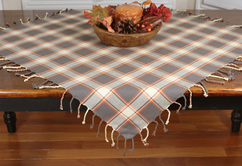 Our gray Fall Sky Table Square featues a plaid of gray, orange, and cream and measures 36"x36" with a hand braided fringe.