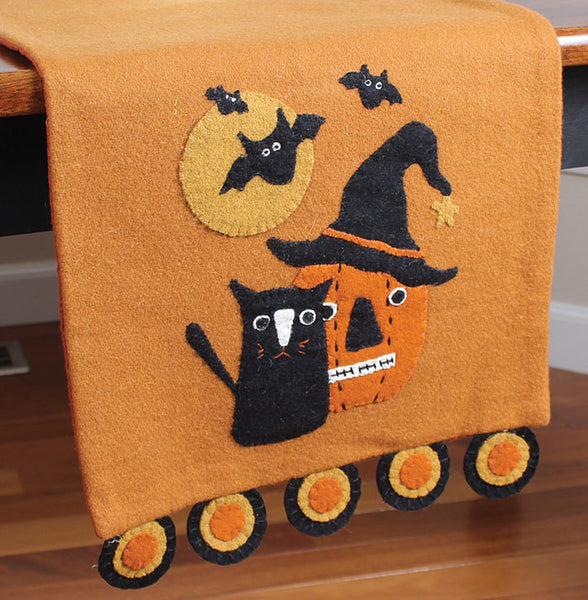 The Cat, Bats, And Pumpkin Felt Runner features pumpkin and cat friends with bat details on an orage background.