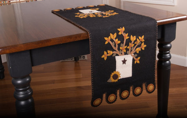 Our black BitterSweet Crock Table Runner features a star crock holding flower with sunflowe detail.